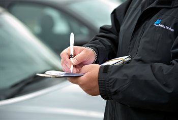 A close up photograph of a Civil enforcement officer writing a ticket