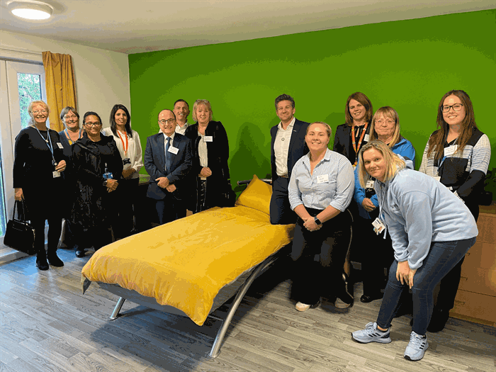 A group of people gather round a single bed at YMCA Borehamwood.