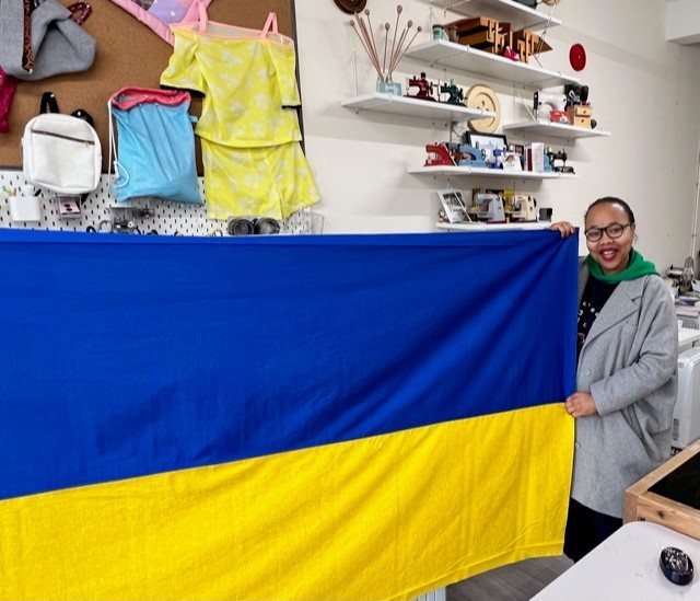A woman holds one side of the flag while standing in a sewing room.
