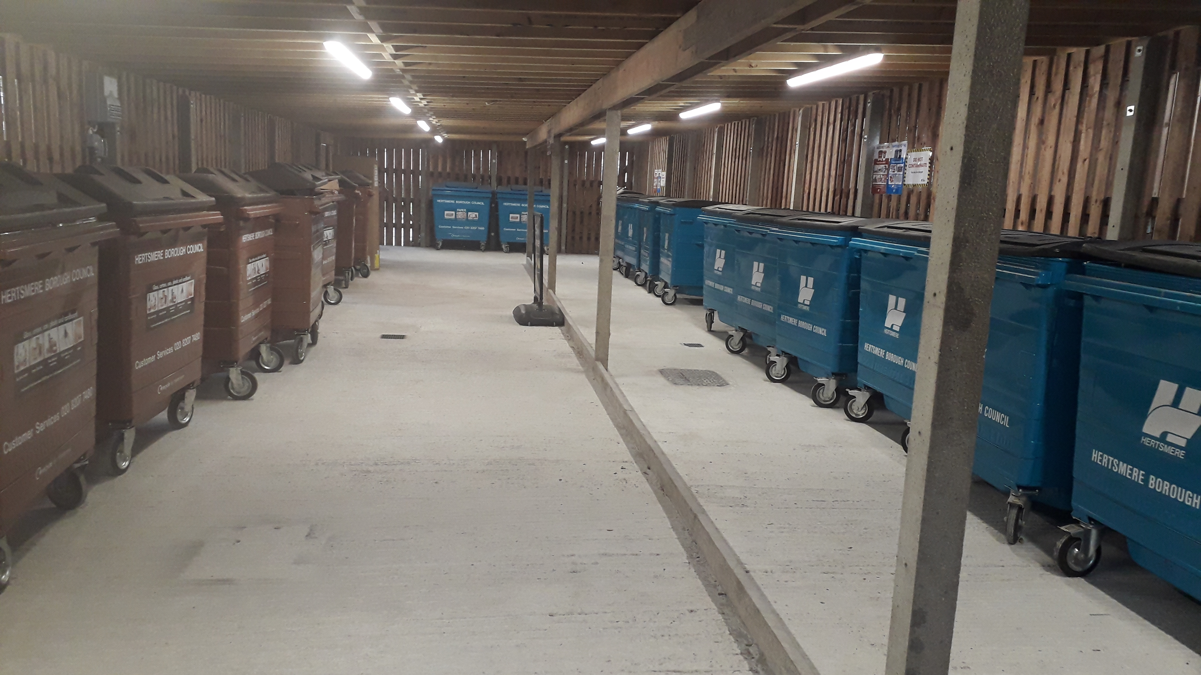 Neatly kept communal bin store with refuse and recycling bins running down each side.