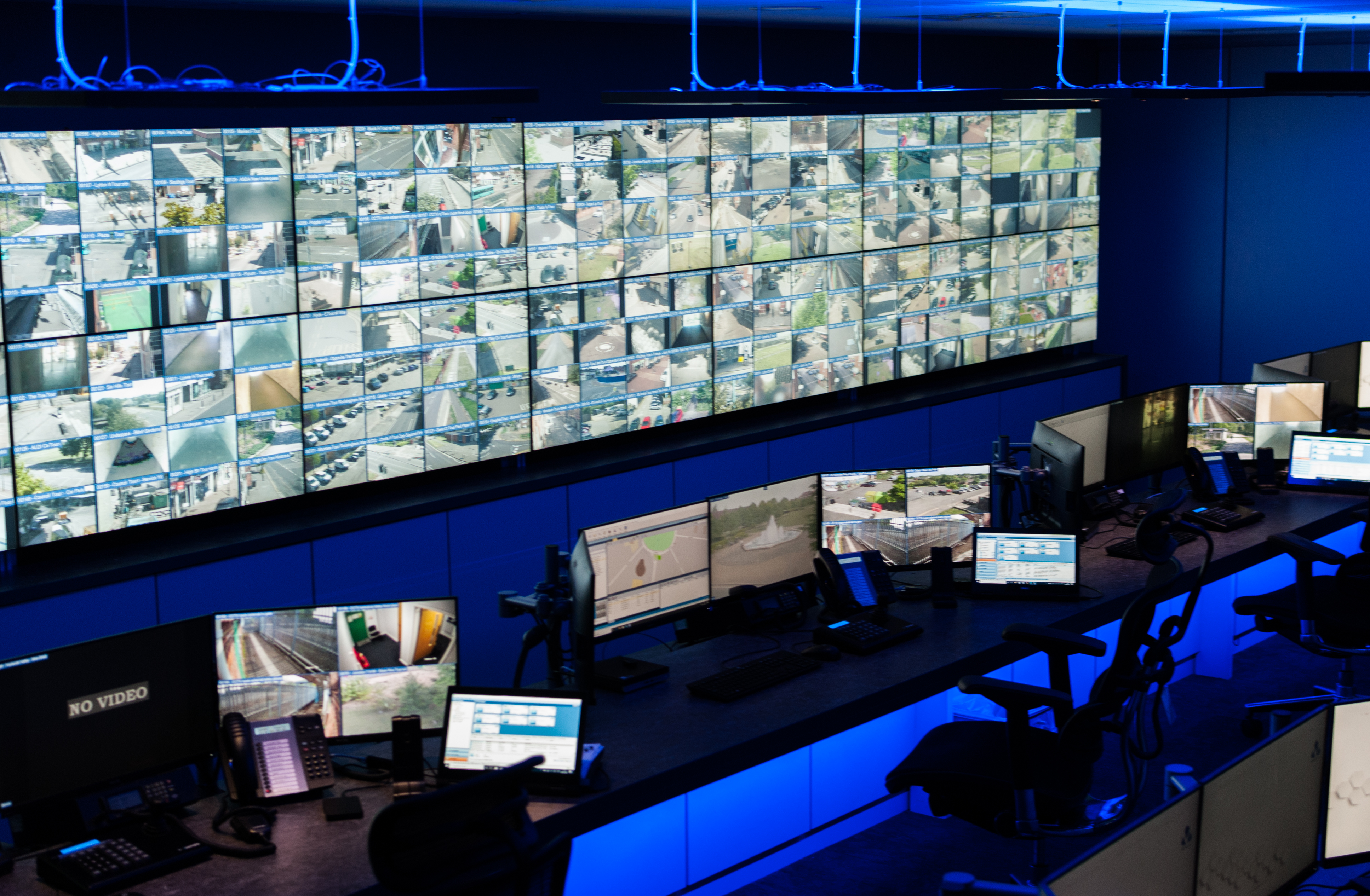 A wall of screens with CCTV images on. Desks are facing this wall.