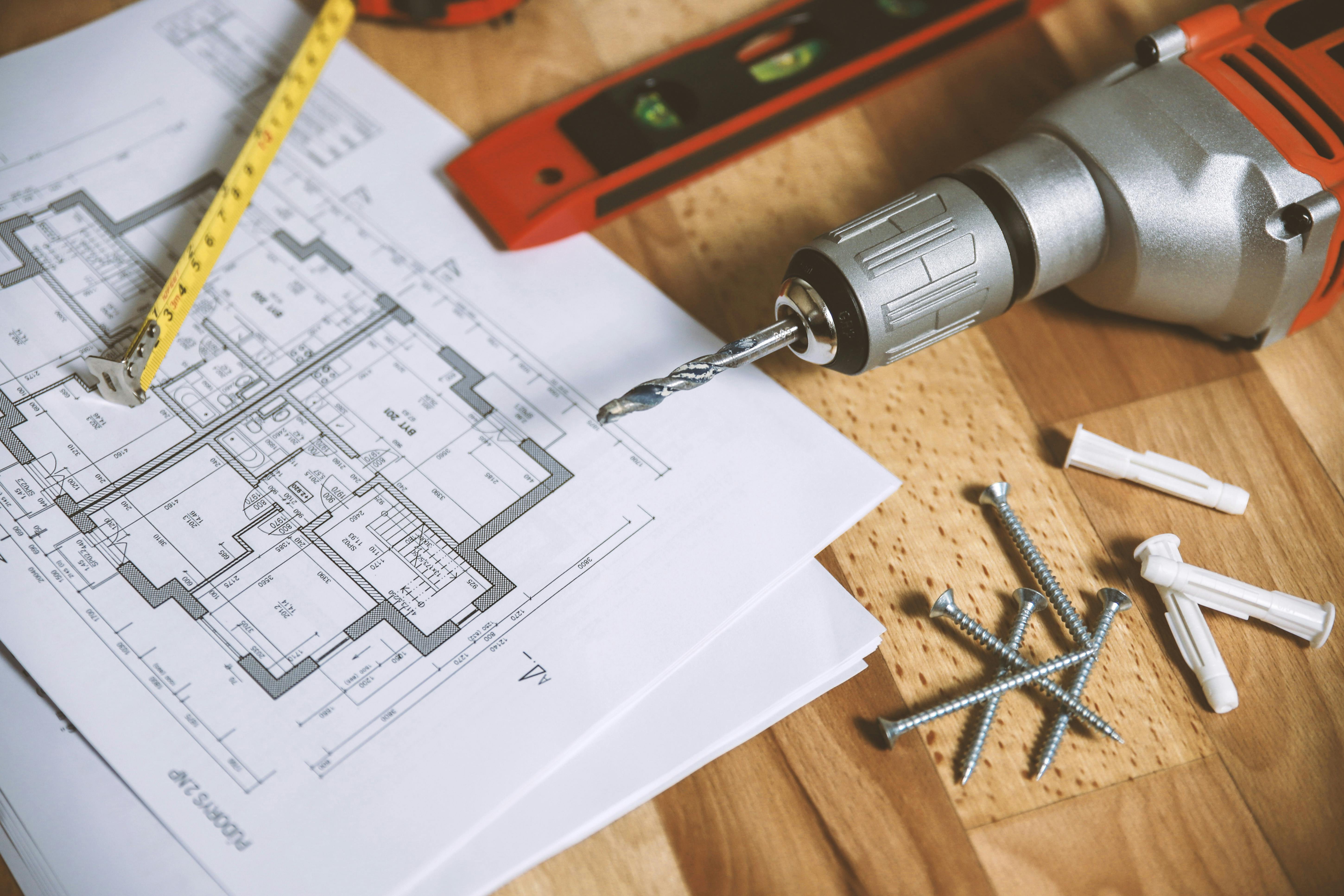 An architect drawing on a desk, surrounded by tools such as nails, a drill and a tape measure. 