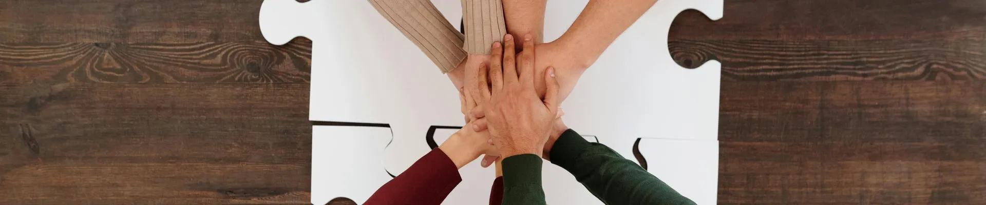 A group of hands meeting together on top of a table with large puzzle pieces.