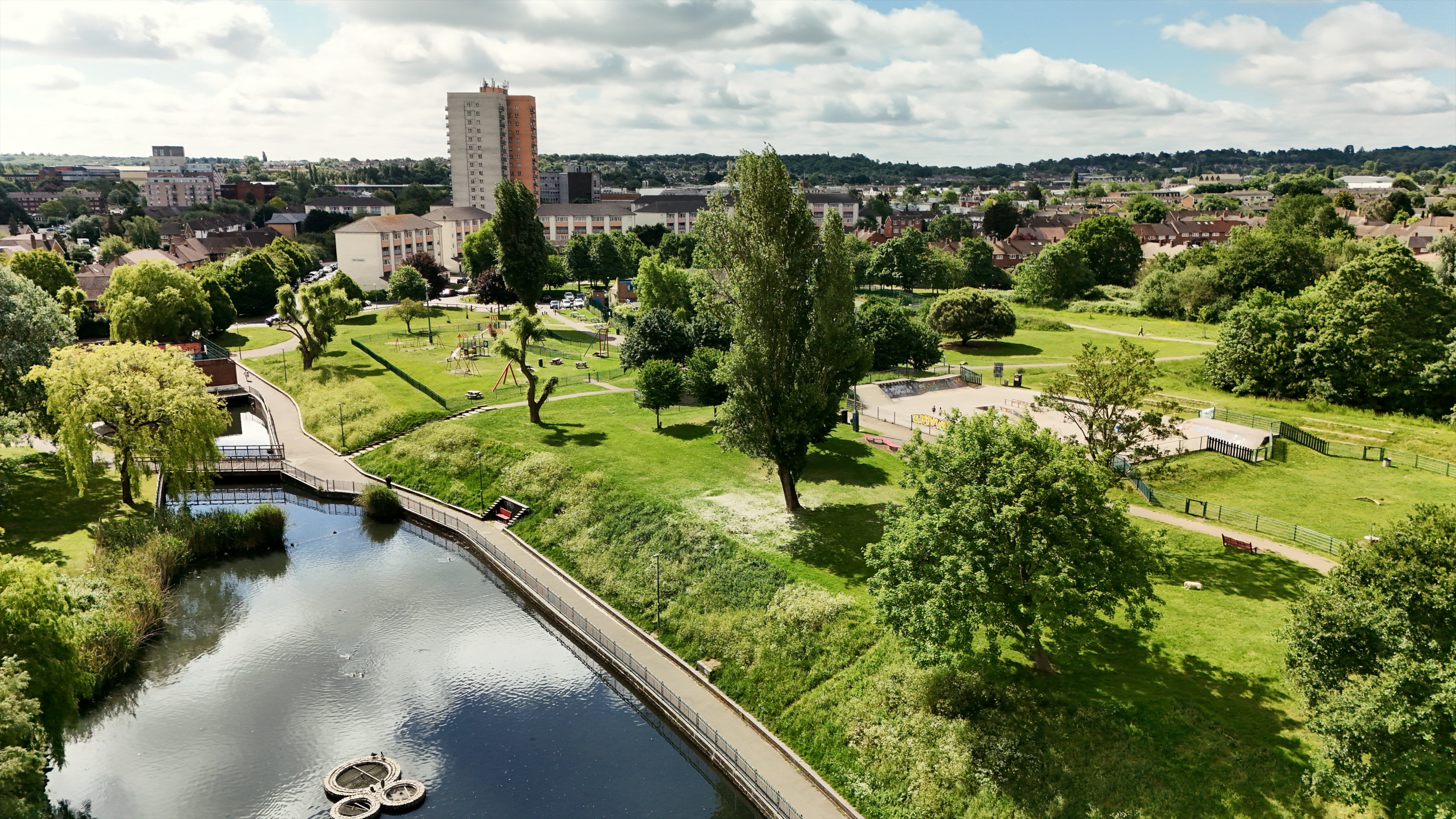 A landscape view of Hertsmere showing a lake, greenery and buildings in the distance. 