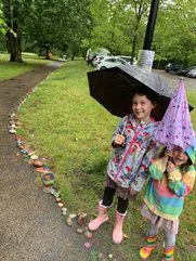 Two children holding umbrellas in the park along their pebble trail.