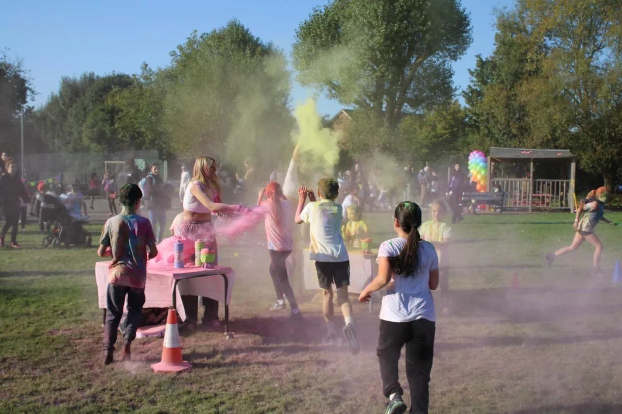Children and adults having a colour run in a field with bursts of colour powder in the air.