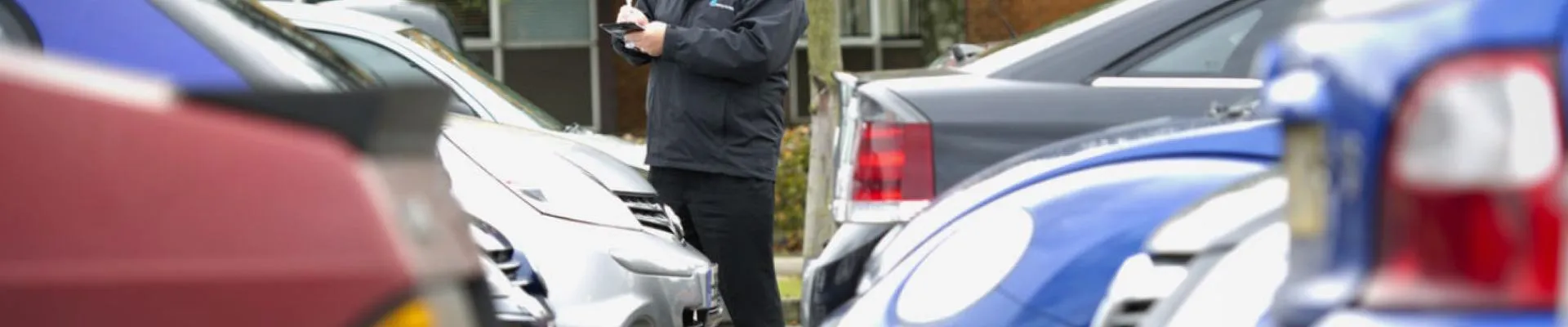 traffic warden standing in car park noting car information