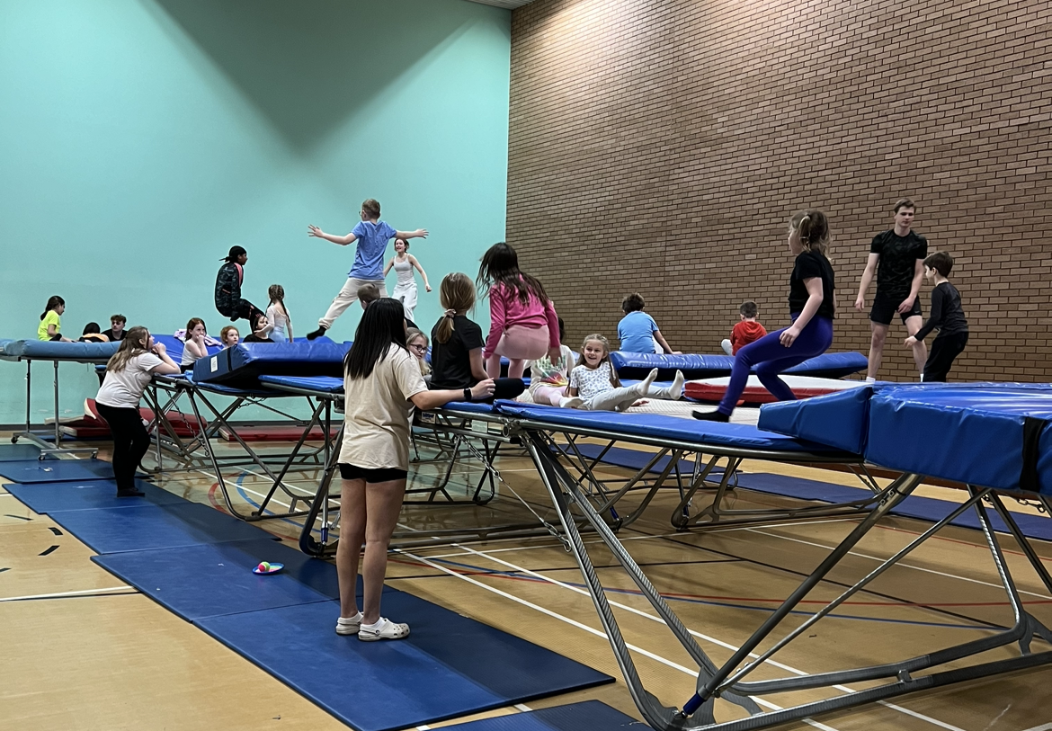 Children learning how to jump on large trampolines with adults helping them. 