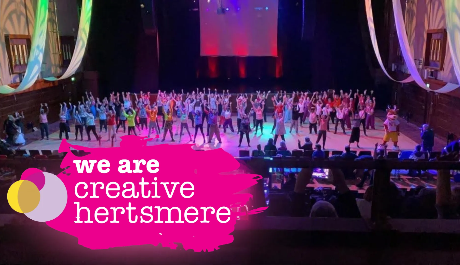 Performers on a stage with the words we are creative Hertsmere in front.
